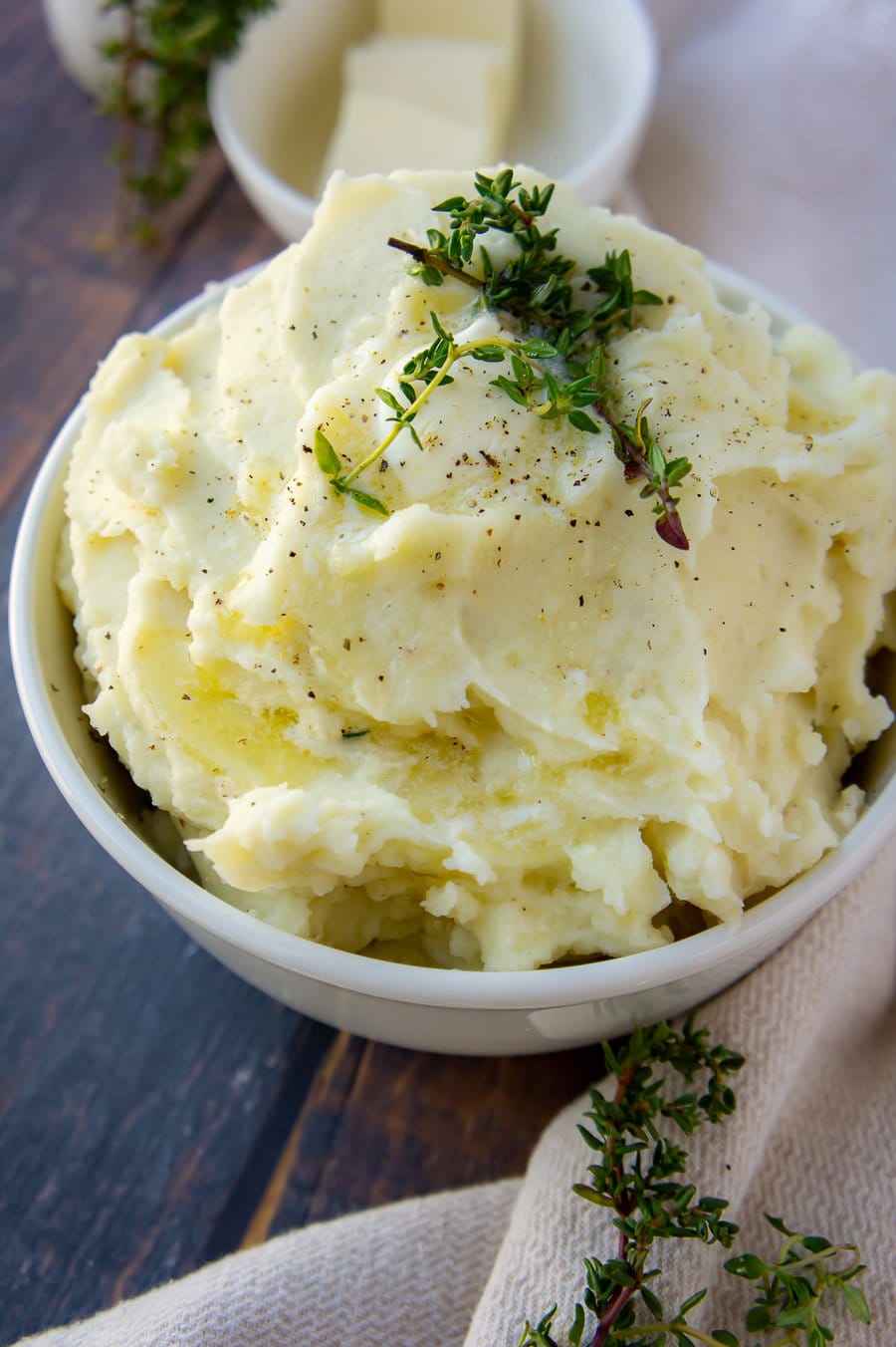 a bowl of creamy mashed potatoes with fresh thyme and butter on top.