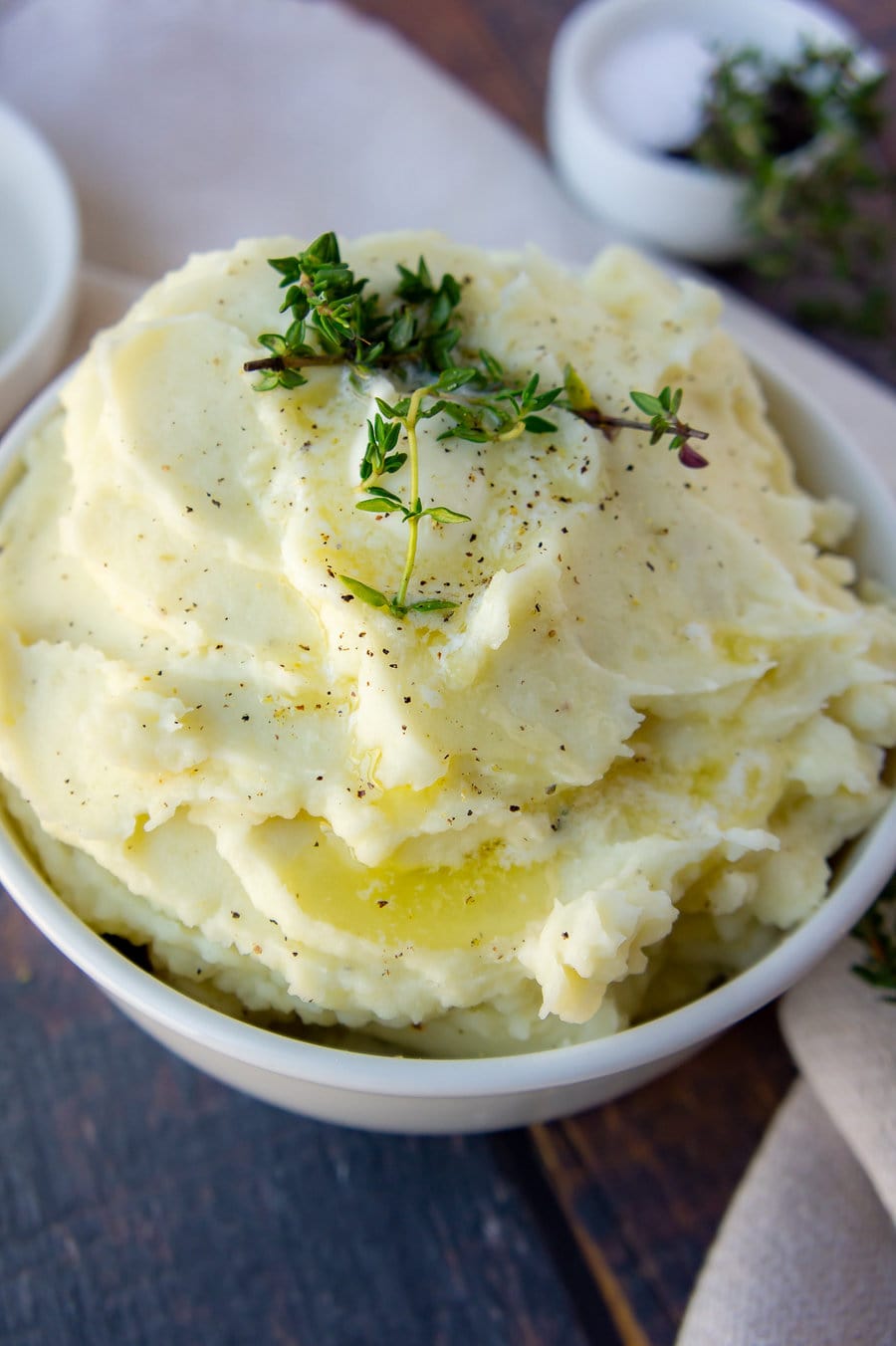 a bowl of mashed potatoes topped with butter, pepper, and fresh thyme sprigs.