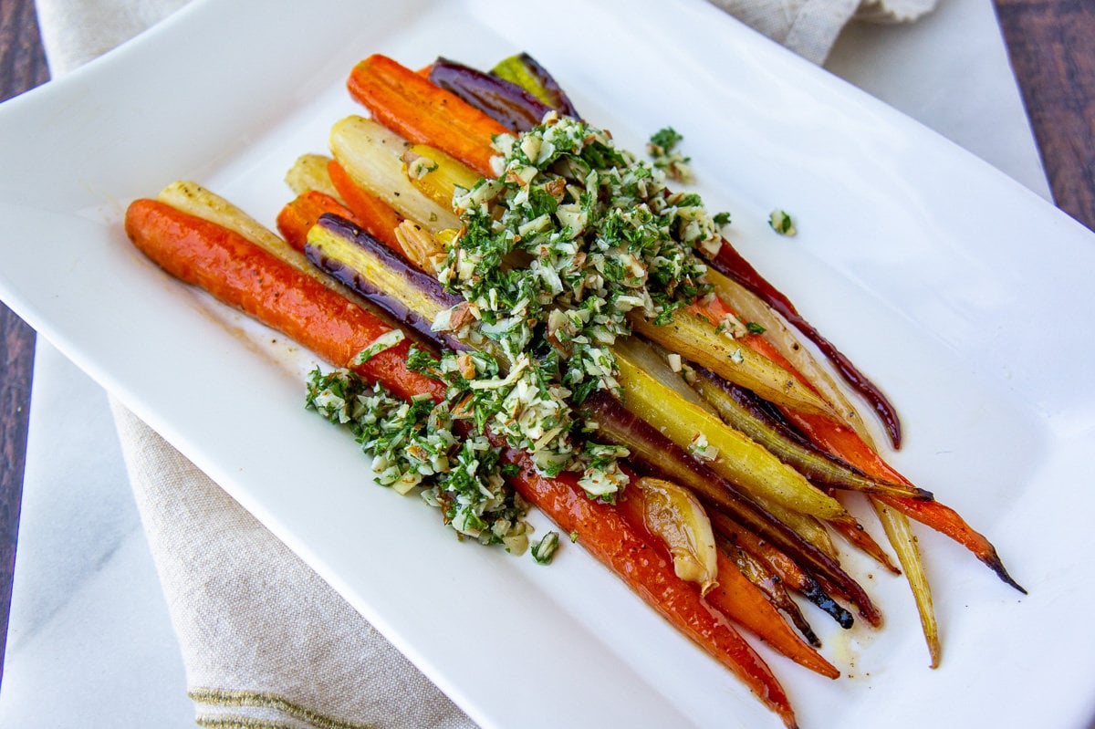a platter of roasted glazed rainbow carrots topped with gremolata.