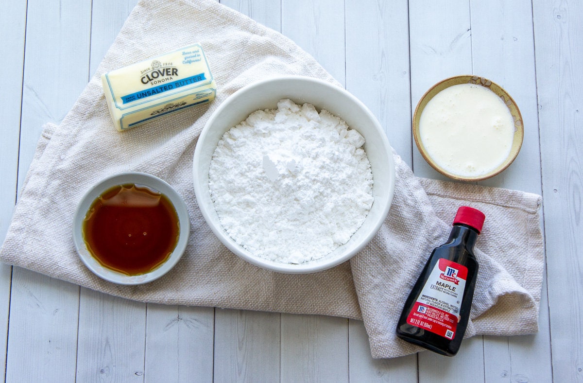 ingredients for maple buttercream including powdered sugar, maple syrup, extract, whipping cream, and butter.