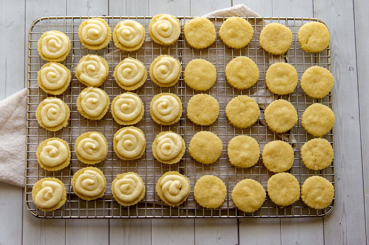 maple sandwich cookies being filled with buttercream on a cooling rack.