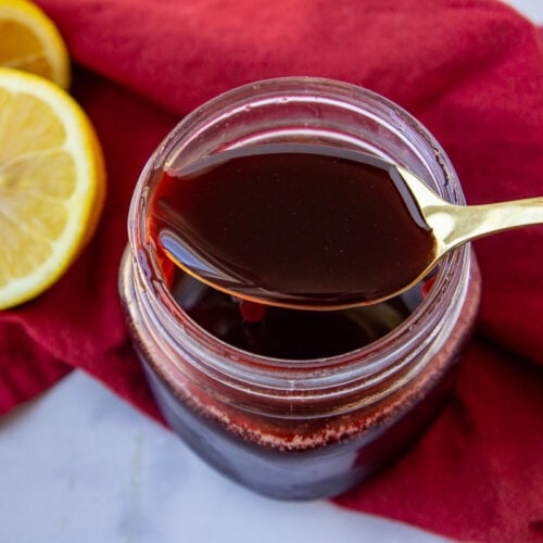 a jar of pomegranate molasses with a gold spoon full on top and a lemon beside it.