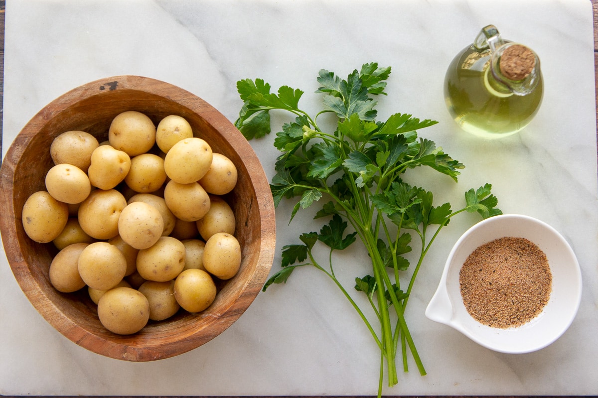 ingredients to make roasted baby potatoes including oil, seasonings, and parsley.
