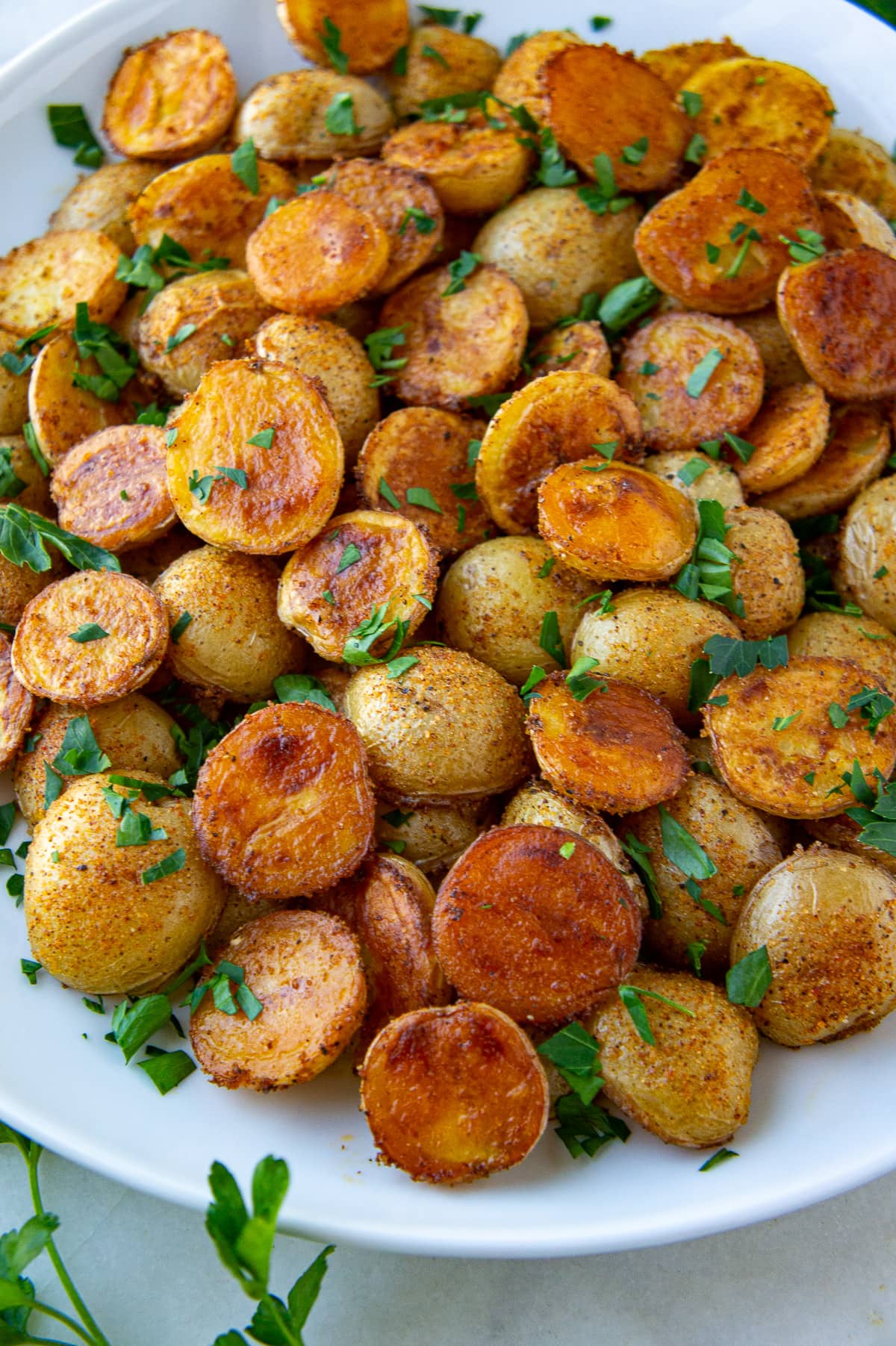 golden brown baby potatoes on a white platter with chopped parsley.