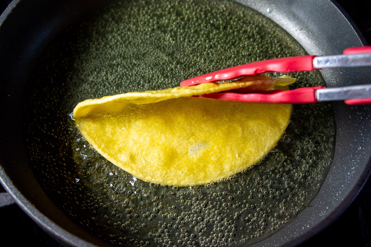 a corn tortilla being crisped in oil.