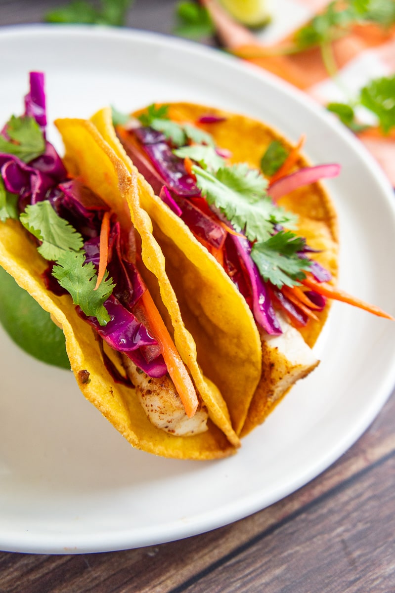 two fish tacos in crispy corn tortillas with cabbage carrots slaw.