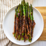 A white plate with grilled prosciutto wrapped asparagus spears.