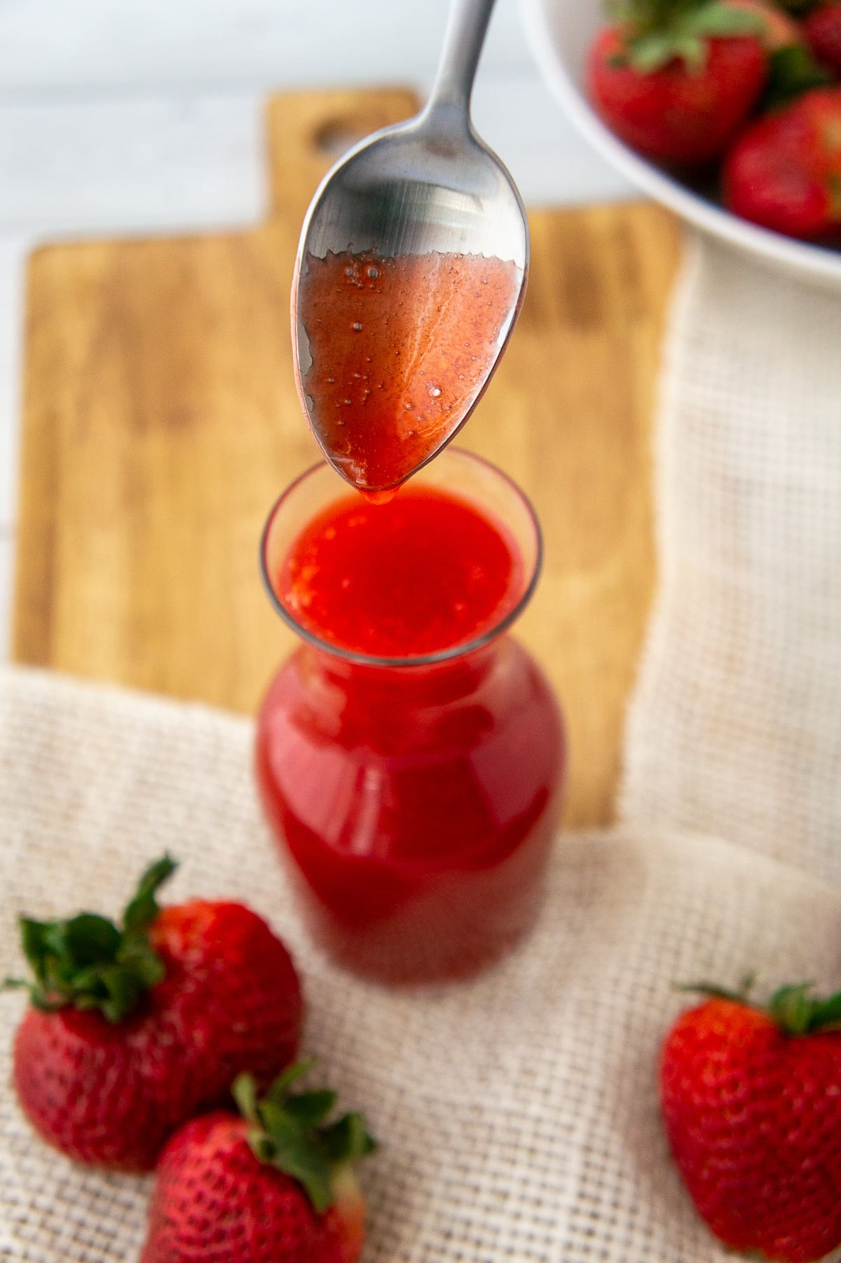 a spoon lifting strawberry sauce from a glass container.