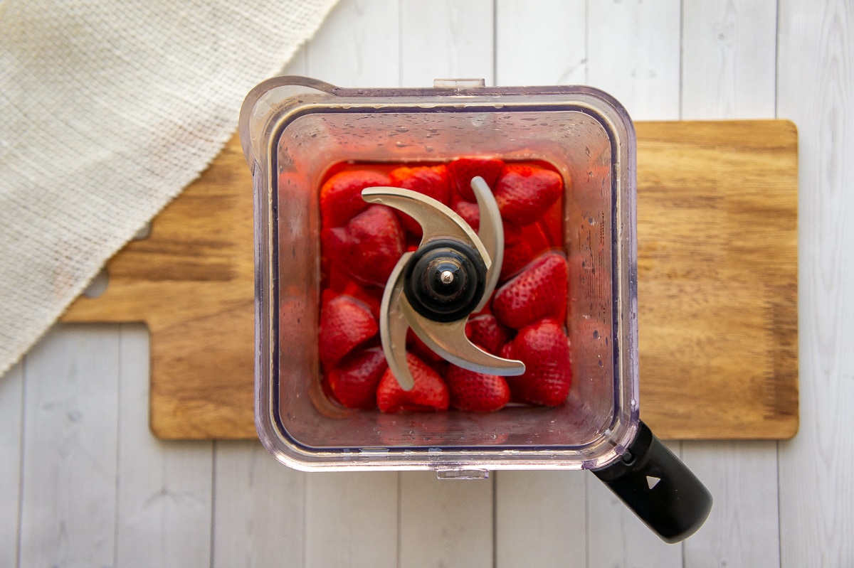 berries and water in a blender on a wooden cutting board.