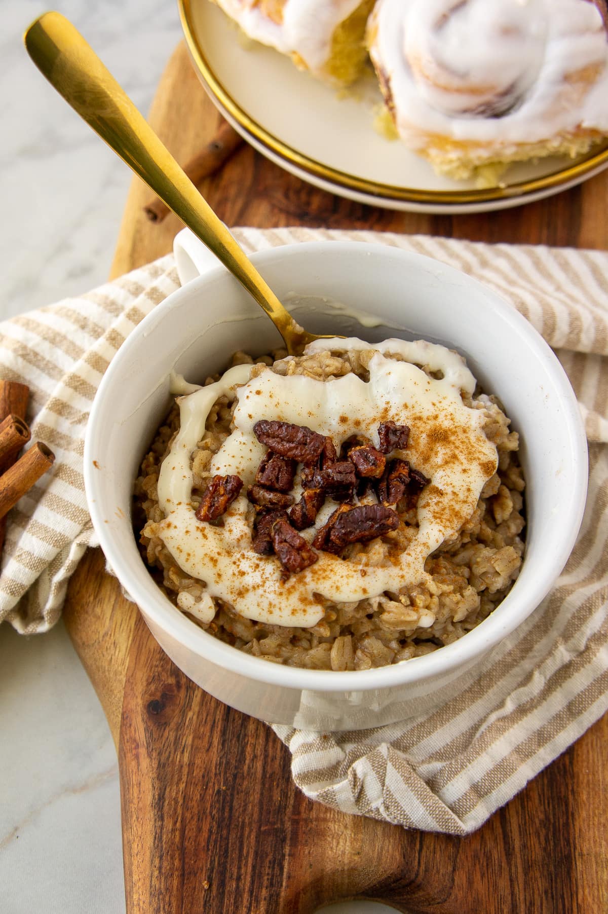 a white bowl of oatmeal with cream cheese icing and chopped pecans on top with a gold spoon.