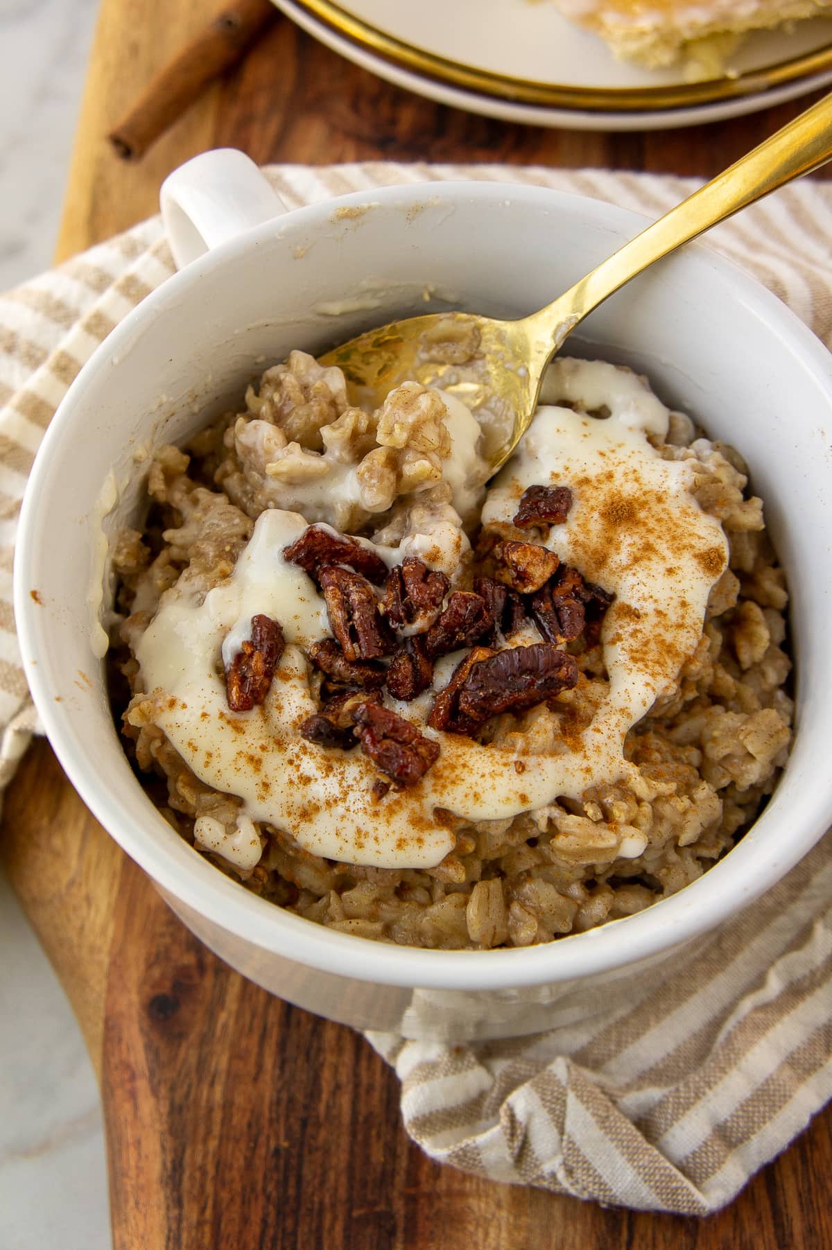 a white bowl with oatmeal, a white icing, and pecans on top with a gold spoon.
