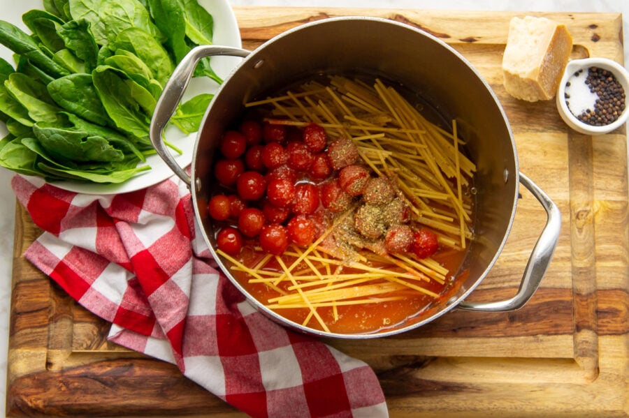 ingredients including dried noodles, cherry tomatoes, water, and seasonings are in the one pot to make pasta.