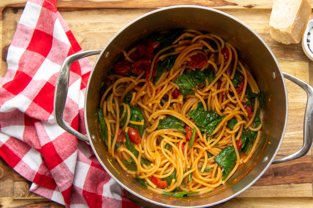 a large pot with cooked pasta, wilted spinach, and cherry tomatoes inside.