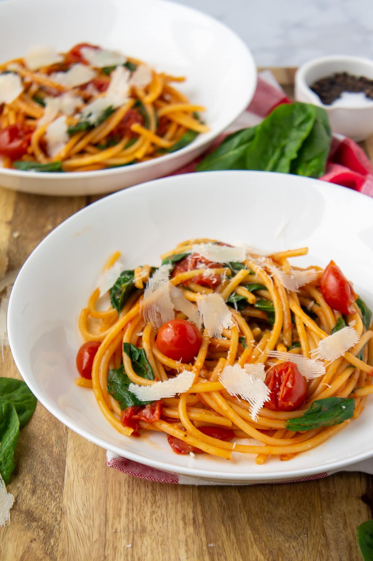 two plates of spinach and tomato pasta with shaved parmesan cheese on top.