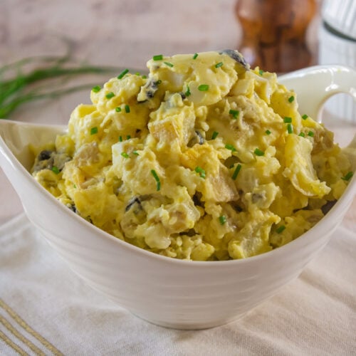 a white bowl of potato and egg salad on a linen napkin.