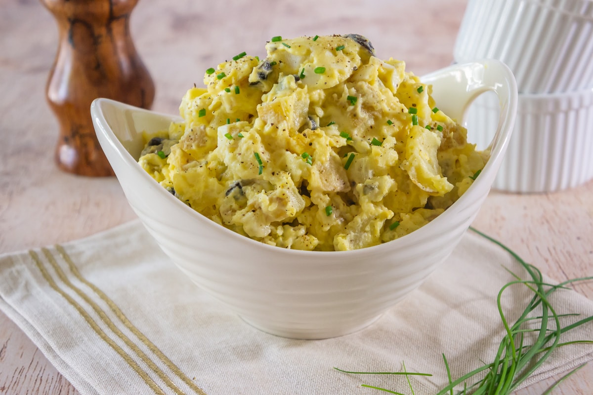 a white bowl on a linen napkin with potato and egg salad inside.