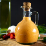 a glass bottle with red creamy mayonnaise inside.