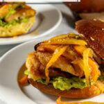 A chicken sandwich with crispy buttermilk cutlets and avocado and peppers on a bun on a white plate.