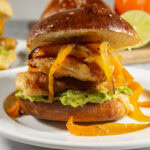 a sandwich of crispy chicken, bell peppers, and avocado on a white plate.