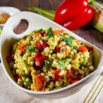 A bowl of corn salad with avocado, red pepper, and herbs.