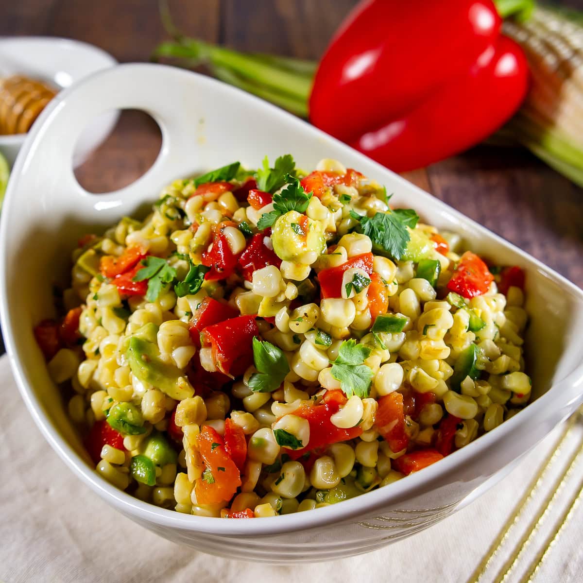 A bowl of corn salad with avocado, red pepper, and herbs.
