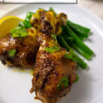 two cooked chicken drumsticks with lemon wedge and green beans on a plate.