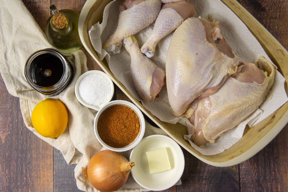 ingredients to make ras el hanout chicken including spices, onion, lemon, raw chicken, and pomegranate molasses.