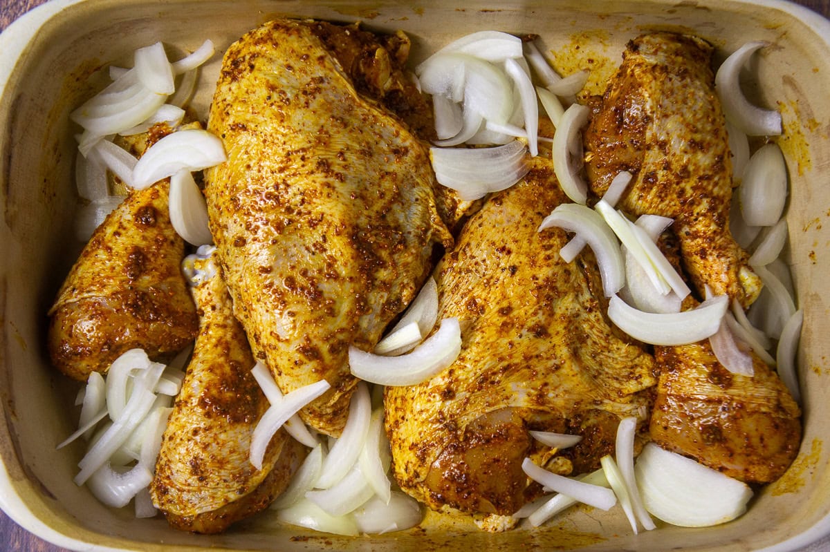 a pan of raw spice rubbed chicken and onions.