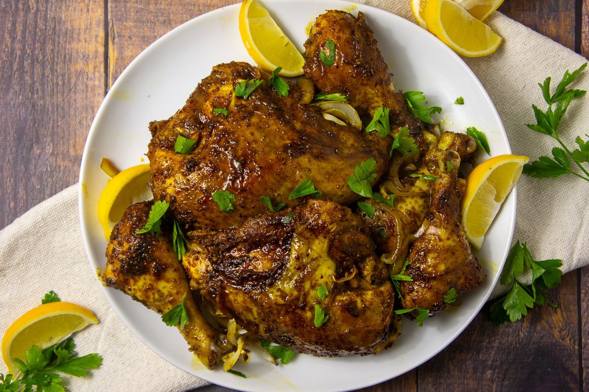 a white platter with spice rubbed roasted chicken on it wiht lemon wedges and parsley.