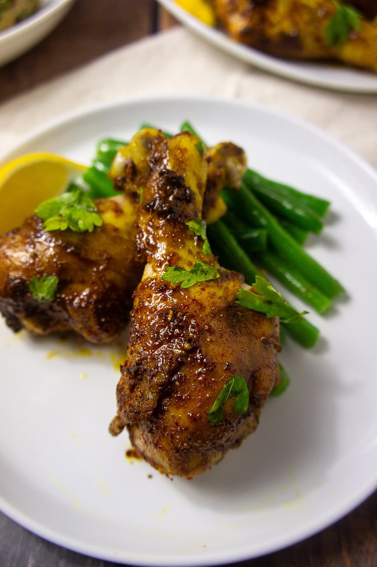 two cooked chicken drumsticks with lemon wedge and green beans on a plate.