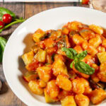a white bowl of tomato basil gnocchi with basil on top.
