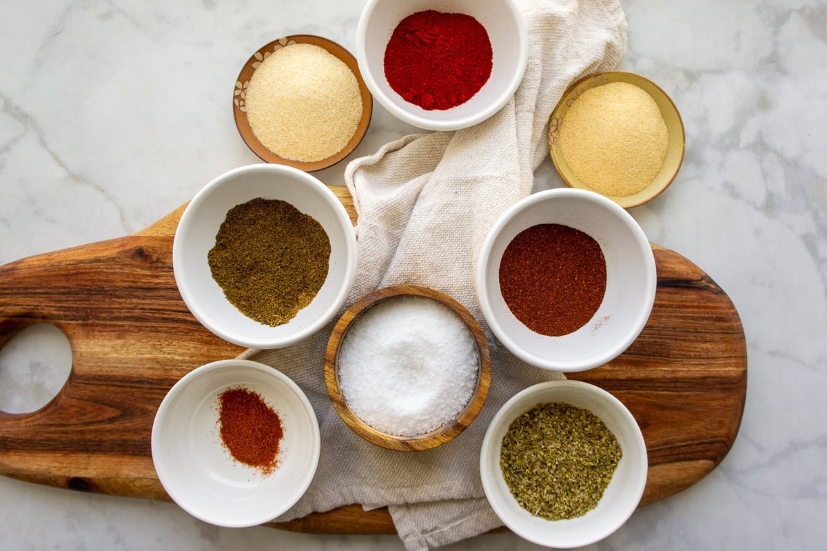 ingredients to making ground beef taco seasoning in small white bowls including chili powder, smoked paprika, onion powder, garlic powder, cayenne, oregano, and salt.