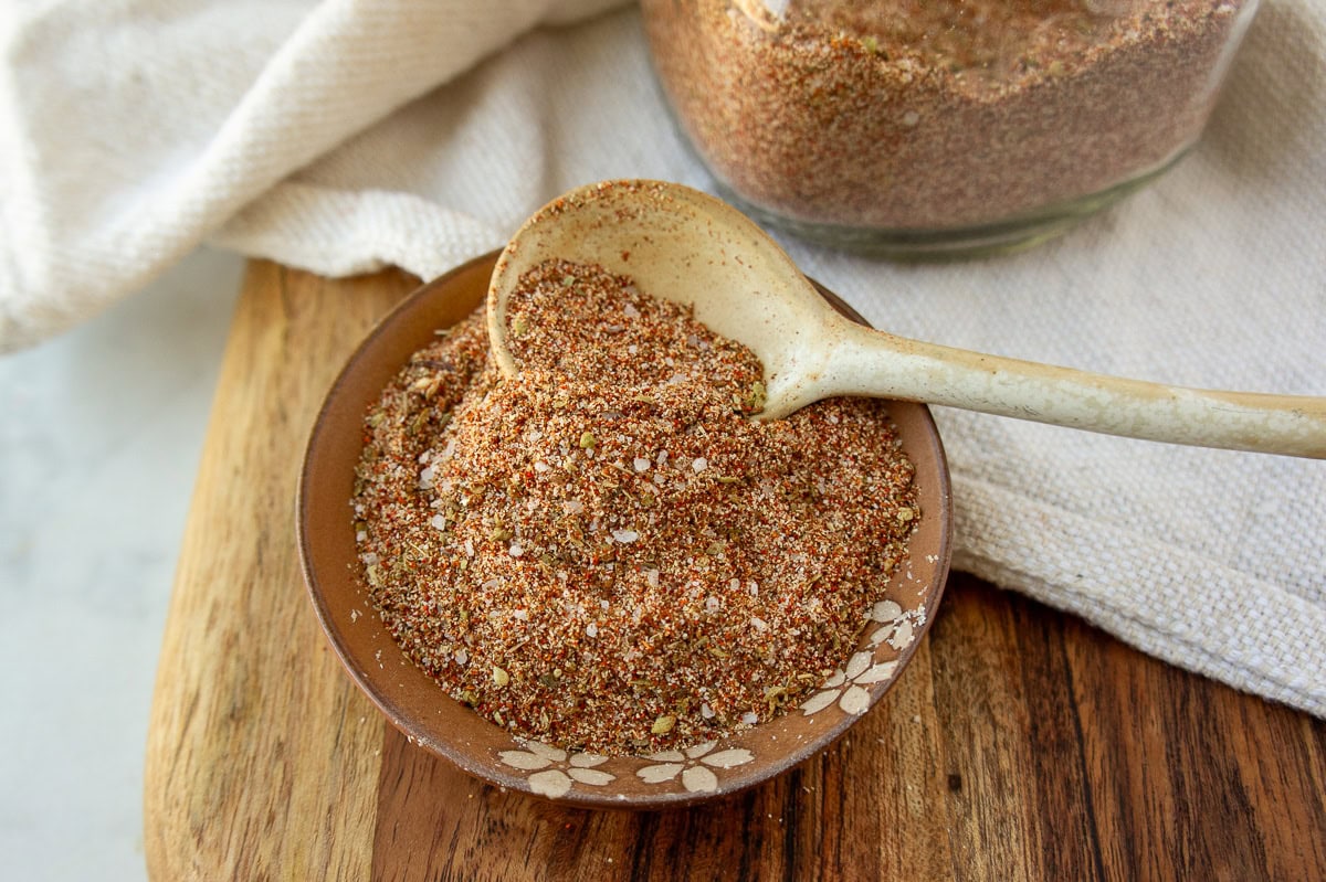 a bowl of taco seasoning on a wooden cutting board with a white spoon inside it.