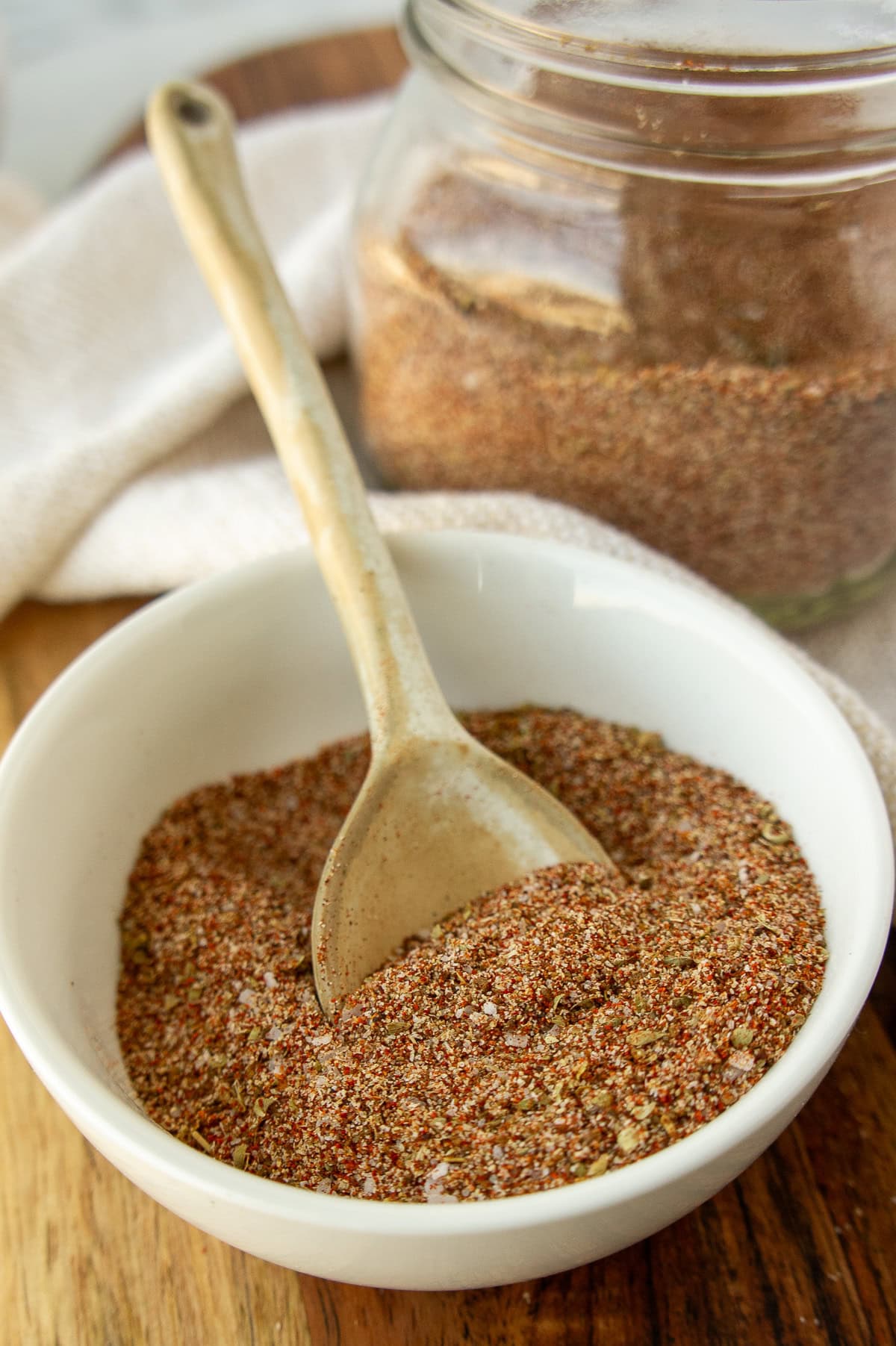 a white bowl of mixed spices with a white spoon and mason jar.