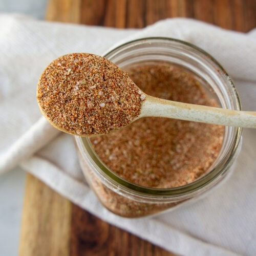 a white spoon of spices sitting across an open mason jar with more spice blend inside.