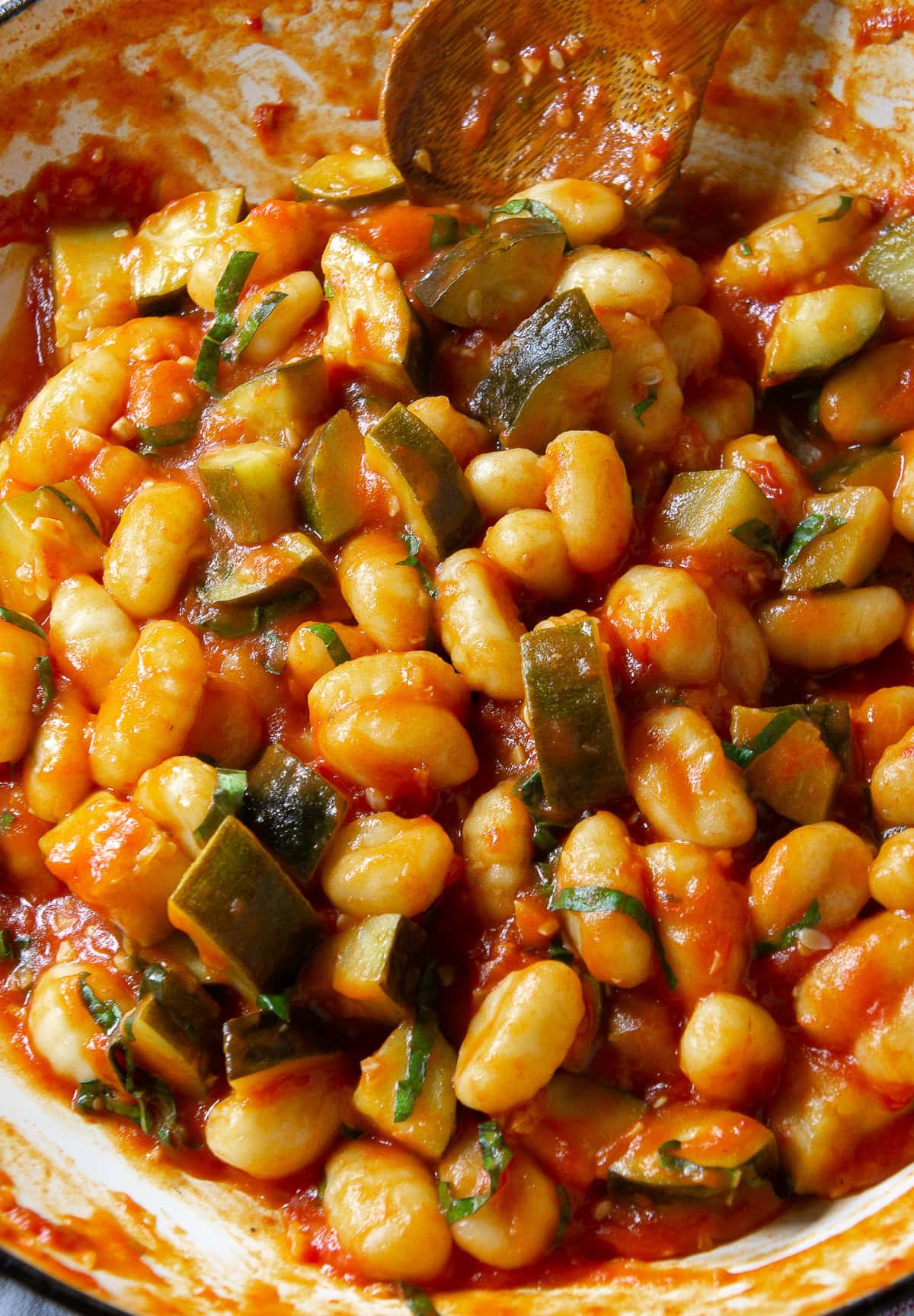 a pan of gnocchi and zucchini cooking in a red sauce.