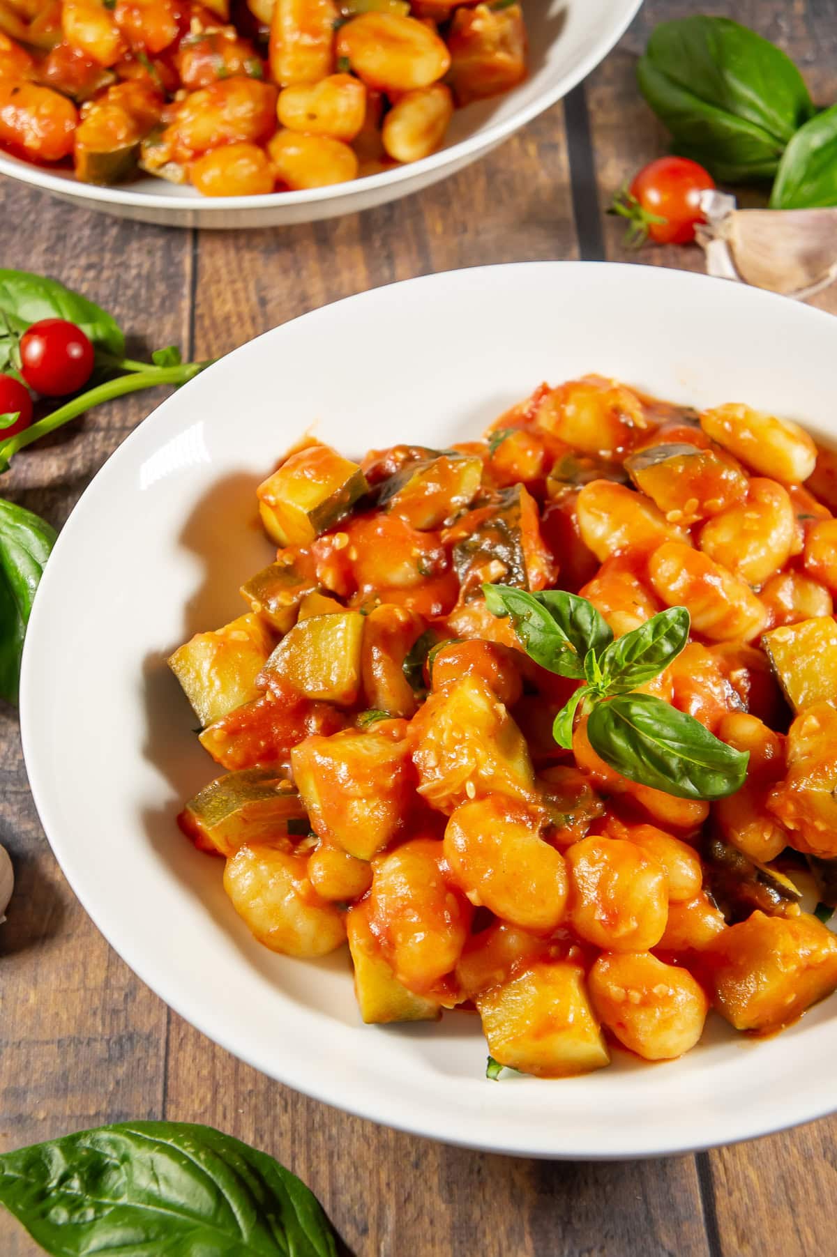 a white bowl of tomato basil gnocchi with basil on top.