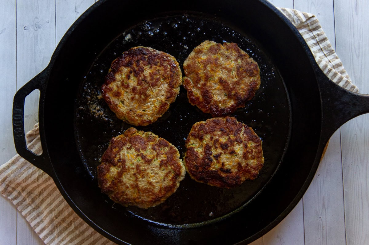 four browned burger patties in a cast iron pan.