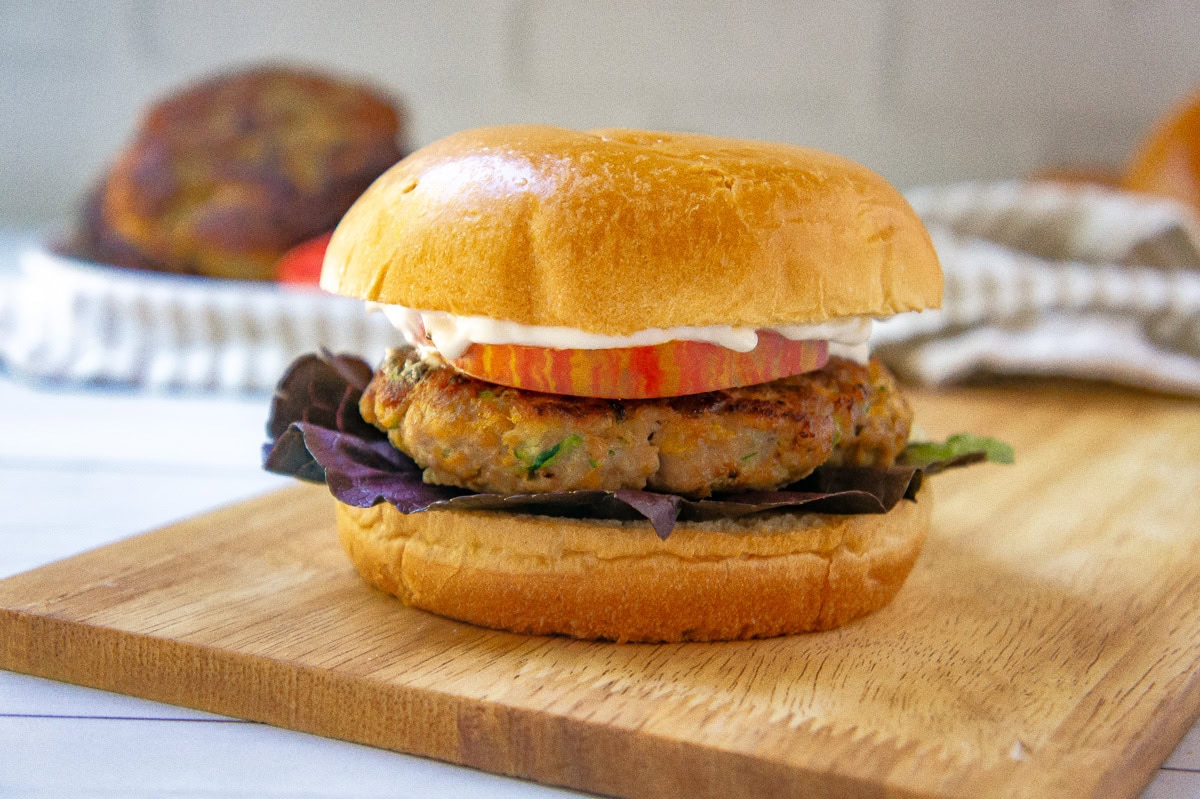 a turkey burger on a brioche bun with tomato, purple lettuce, and mayo on a cutting board.