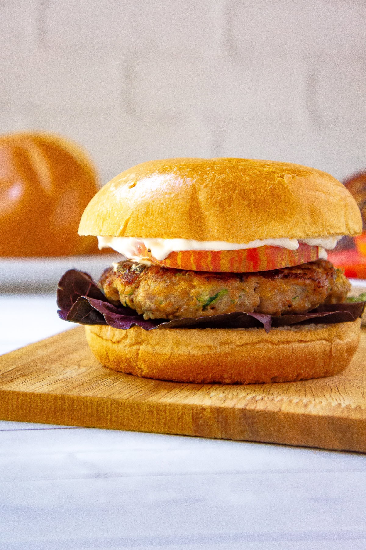 a turkey burger on a brioche bun with tomato, purple lettuce, and mayo on a cutting board.