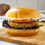 a turkey burger on a brioche bun with tomato, purple lettuce, and mayo on a cutting board.