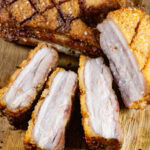 a piece of pork belly roasted crisp and sliced on a wooden cutting board.