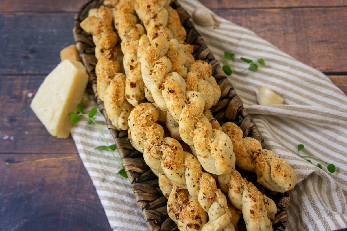 a platter of twisted breadsticks topped with herbs and browned cheese.